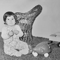 a black and white photo of a baby sitting in front of a wicker chair