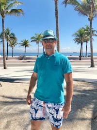 a man wearing a hat and shorts in front of palm trees