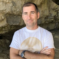 a man in a white t - shirt standing in front of a cave