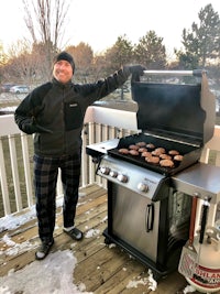 a man standing in front of a grill with burgers on it