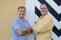 two men standing in front of a yellow and black chevron wall