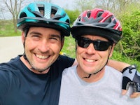 two men wearing helmets pose for a selfie