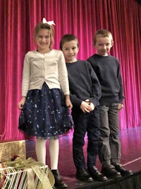 three children standing on stage with presents in their hands