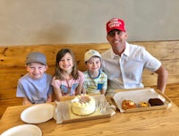 a man with a hat and two children in front of a table with a cake