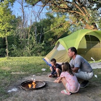 a family sits around a campfire in front of a tent